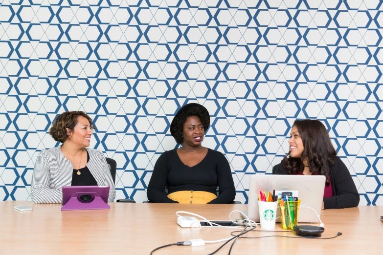 three women sit in front of laptops at a table