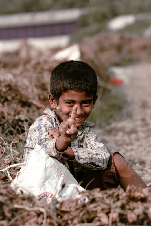 a boy sitting down and pointing to the camera