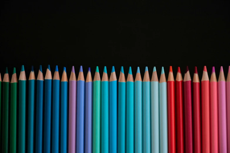 colorful pencils lined up in a horizontal row on a dark surface