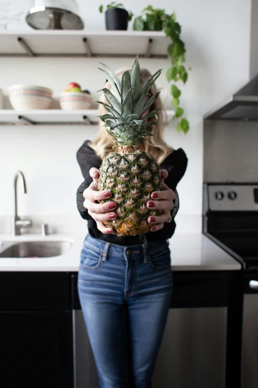 a girl holding up a large pineapple in a kitchen