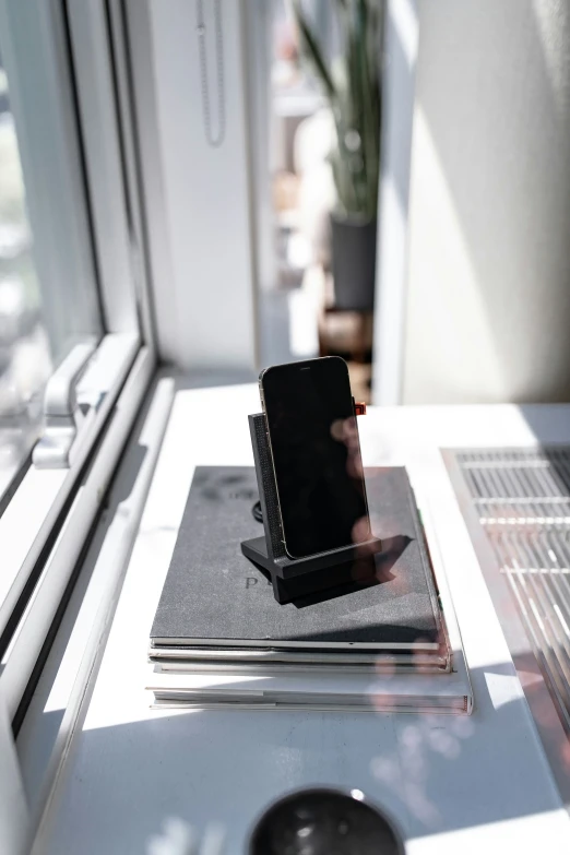 a mobile phone charging on a tablet next to a window