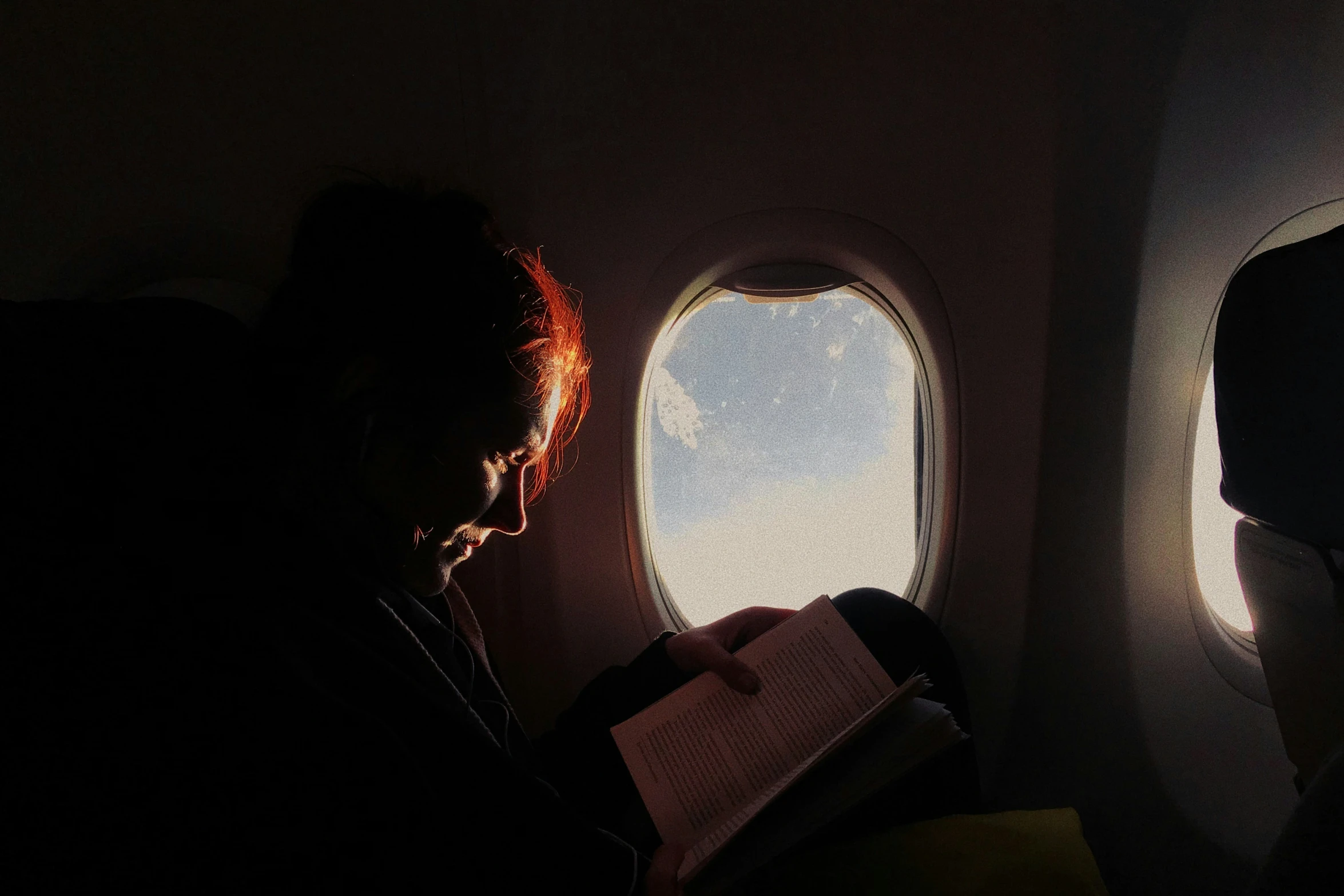 a person reading on a plane with an airplane window