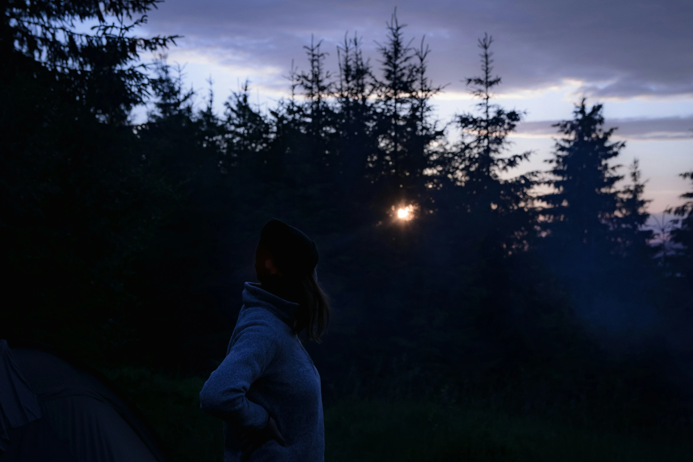 a woman stands next to her tent in the dark