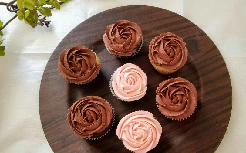 six cupcakes with icing and frosting on a brown and white plate