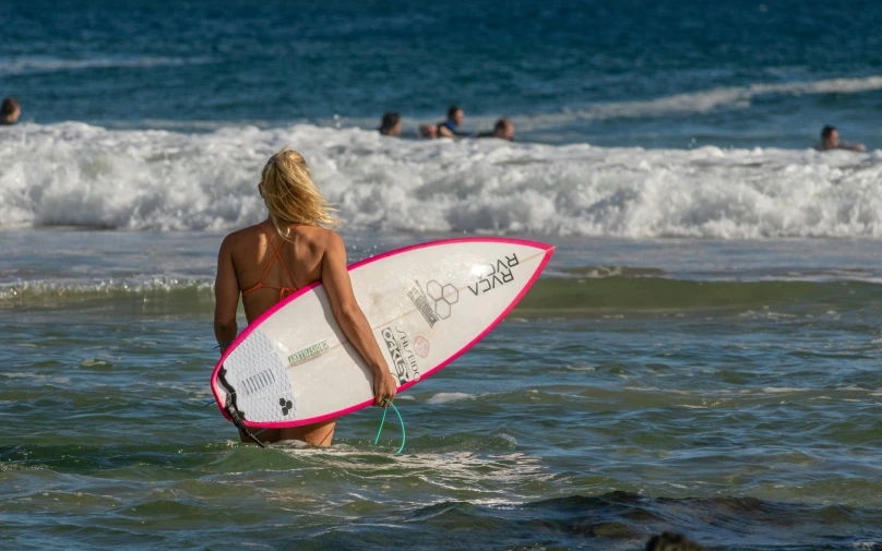a woman walking through the ocean with a surfboard