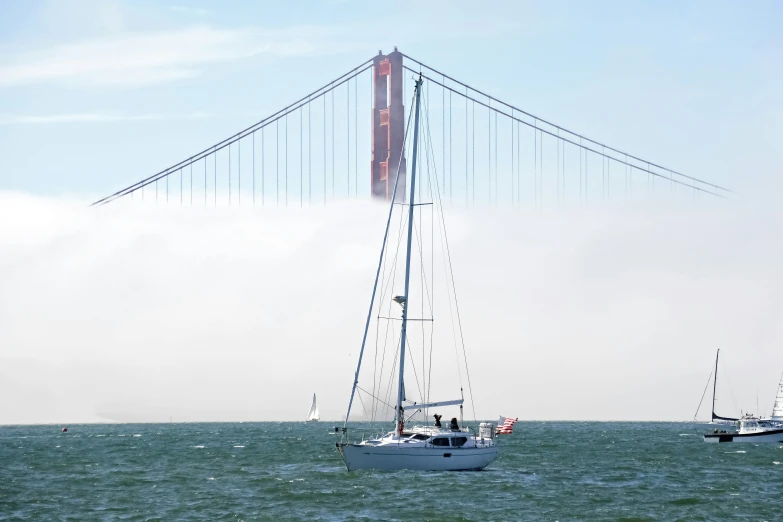 three boats are out in the water and the tall bridge is near the ocean