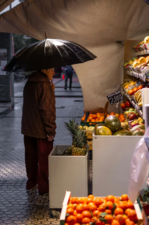 a woman under an umbrella standing near fruit in boxes