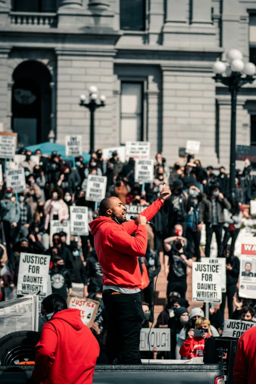 a man in red hoodie on stage speaking at rally