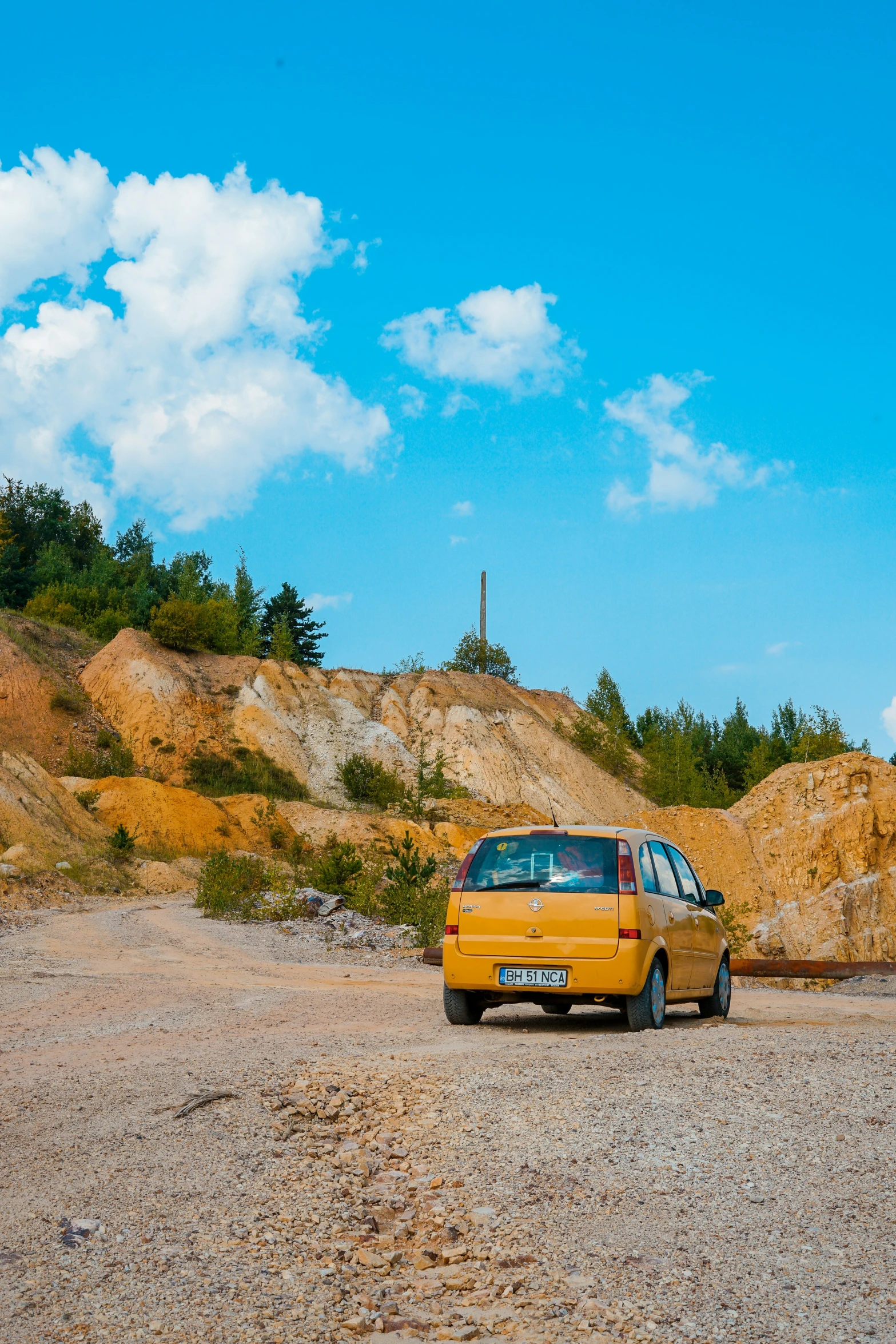 yellow car on gravel road on partly cloudy day