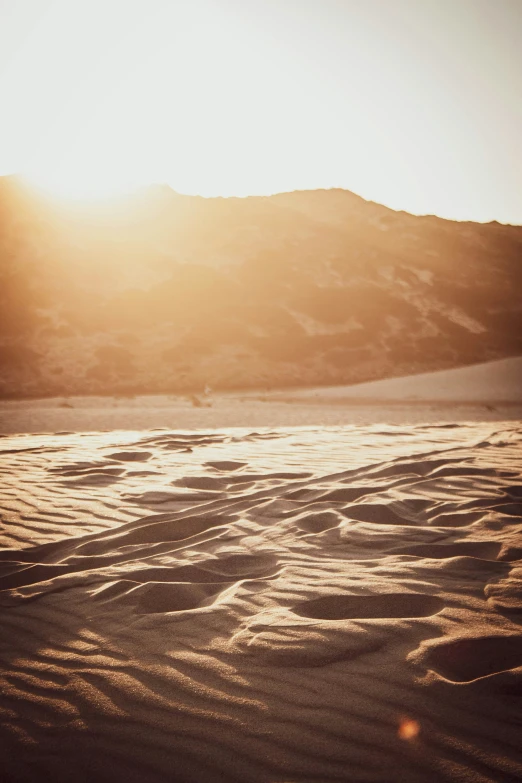 a sandy area surrounded by hills and a mountain at sunset