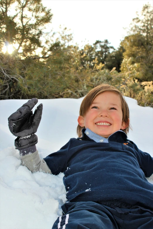 a child lies in the snow outside in the sun