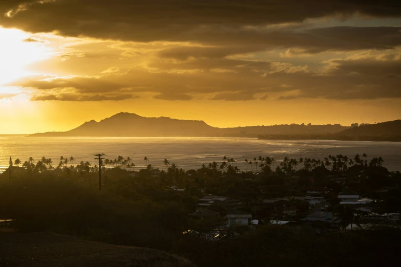 a sunset over the ocean with trees and a hill