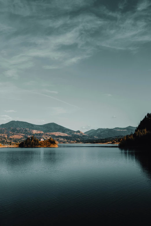 lake surrounded by a forest and mountains under a cloudy sky