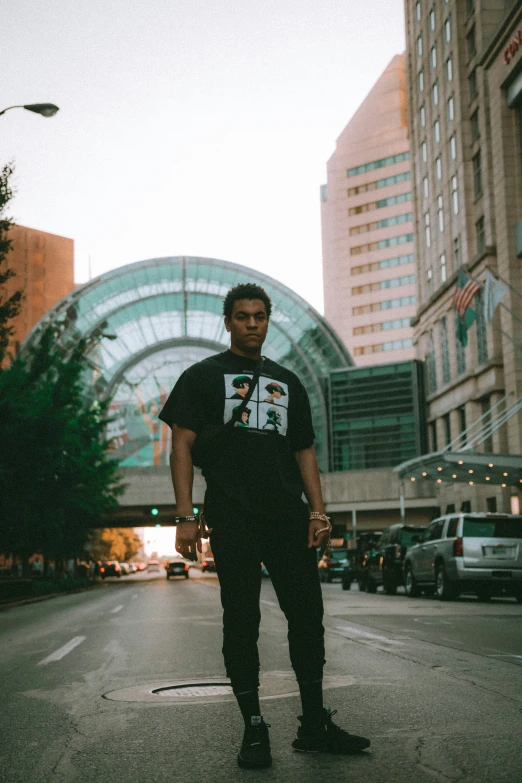 a man in a t - shirt stands on the street with a skateboard