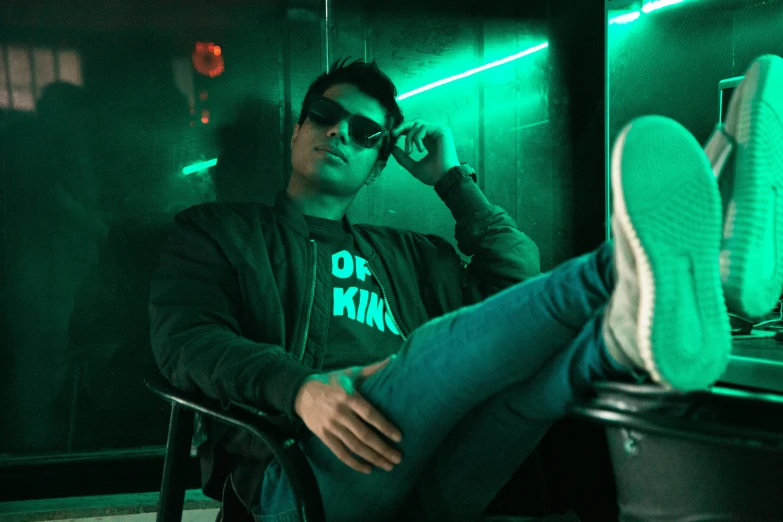 a person in sunglasses sits in a chair while wearing a neon jacket and tennis shoes