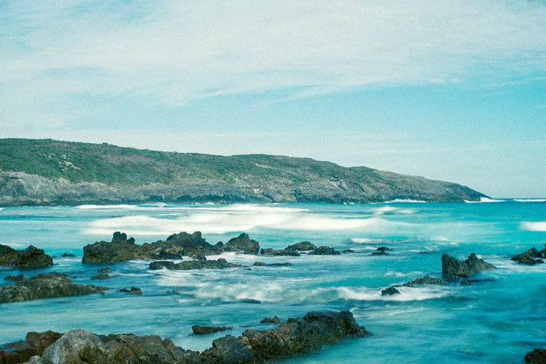 waves are coming in over some large rocks on the ocean