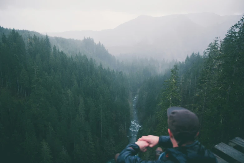 man sitting on deck overlooks trees and rapids