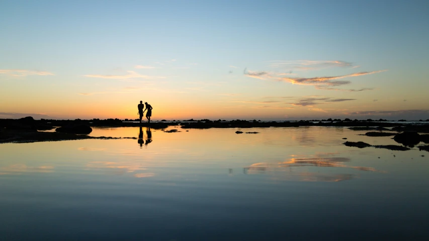 two people standing in the distance at sunset