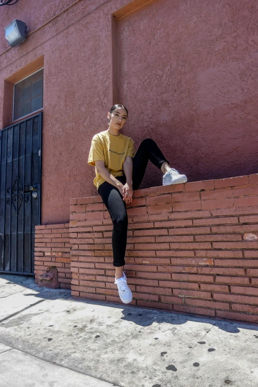 a woman is sitting on a brick wall, looking to the right