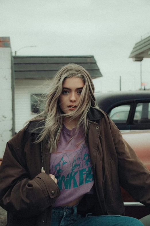 a woman in jacket leaning on truck wearing t - shirt