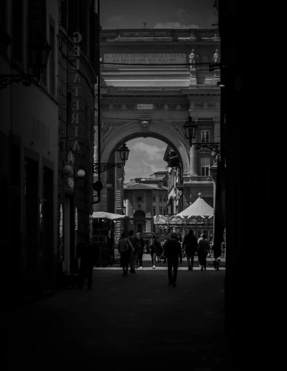 a group of people walk down a street under an arch