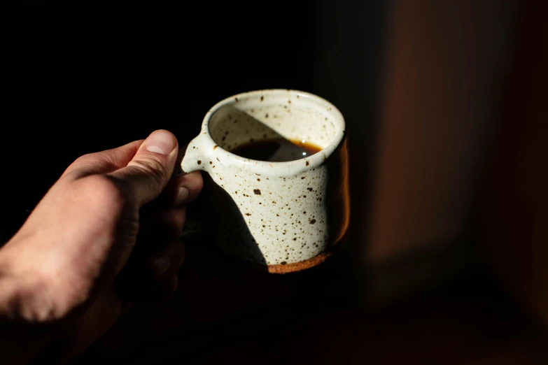 a hand holding a white cup with coffee in it