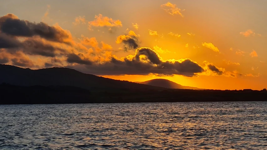 an ocean sunset over some hills