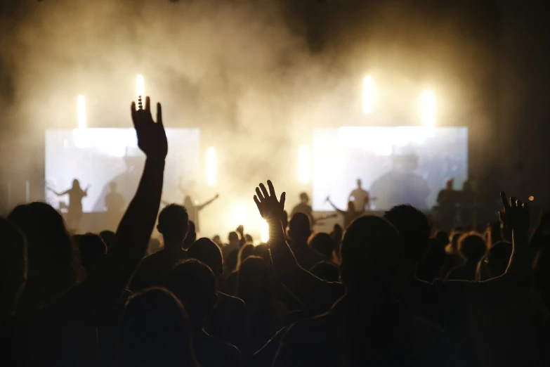 people at concert with their hands raised and lights on