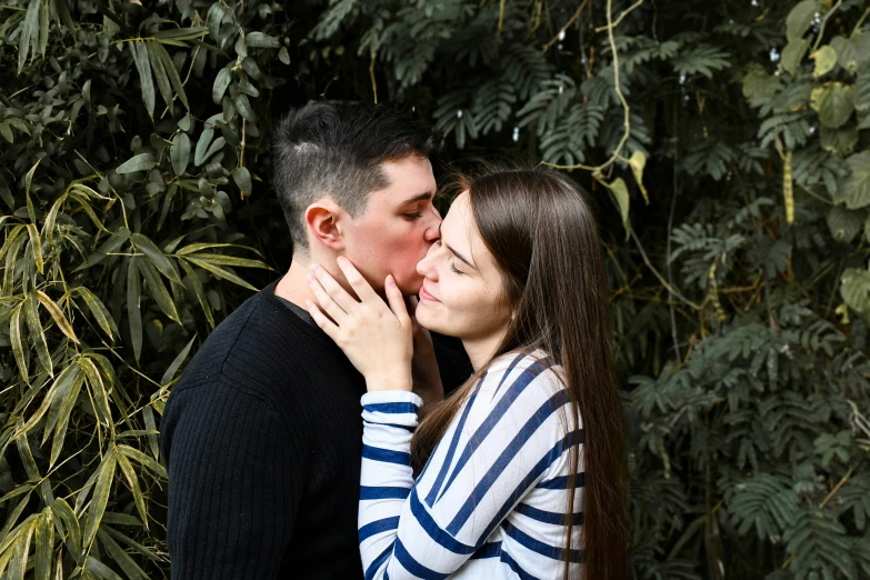 a man and woman kissing in front of leaves