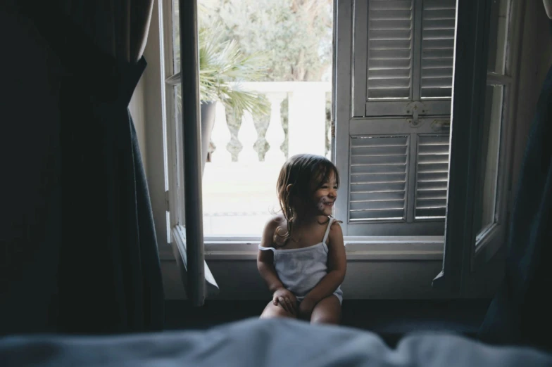 a little girl sitting by a window smiling