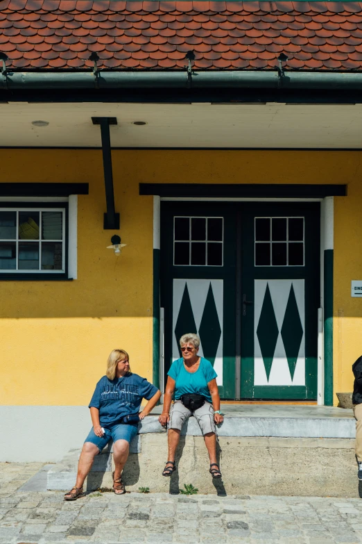 two women sitting on a bench next to a building