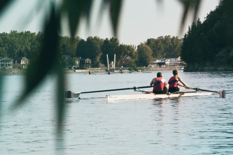 two people in red shirts rowing a boat across water