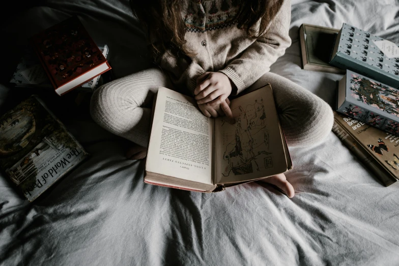 a person reading a book sitting on top of a bed