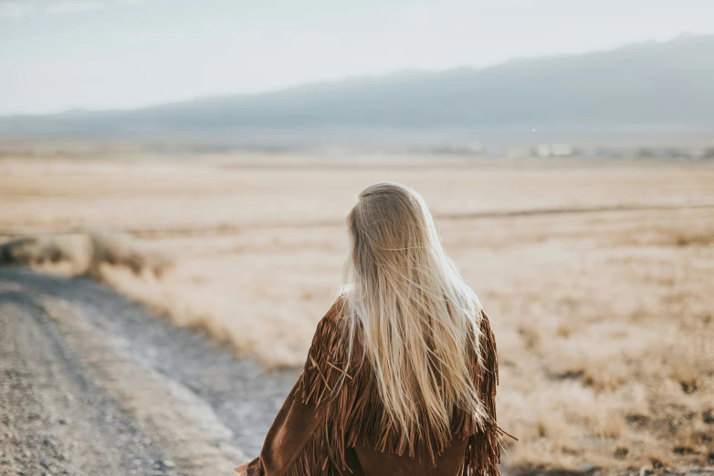 a blonde haired woman wearing a long brown coat walking down a road