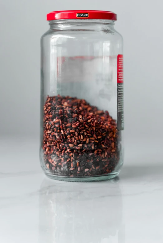 a jar full of red seeds sitting on a white table