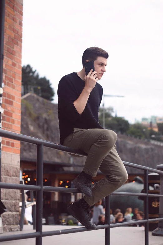 man sitting on railing using cell phone with outdoor restaurant in background