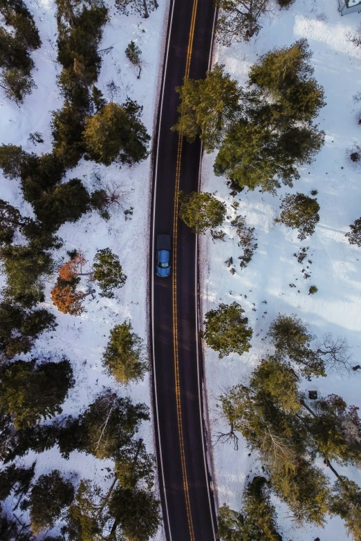 an aerial po of a road in winter with a blue car driving on it