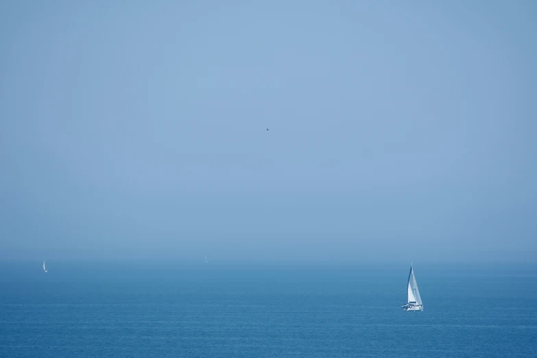 a sail boat floating across the ocean under a blue sky