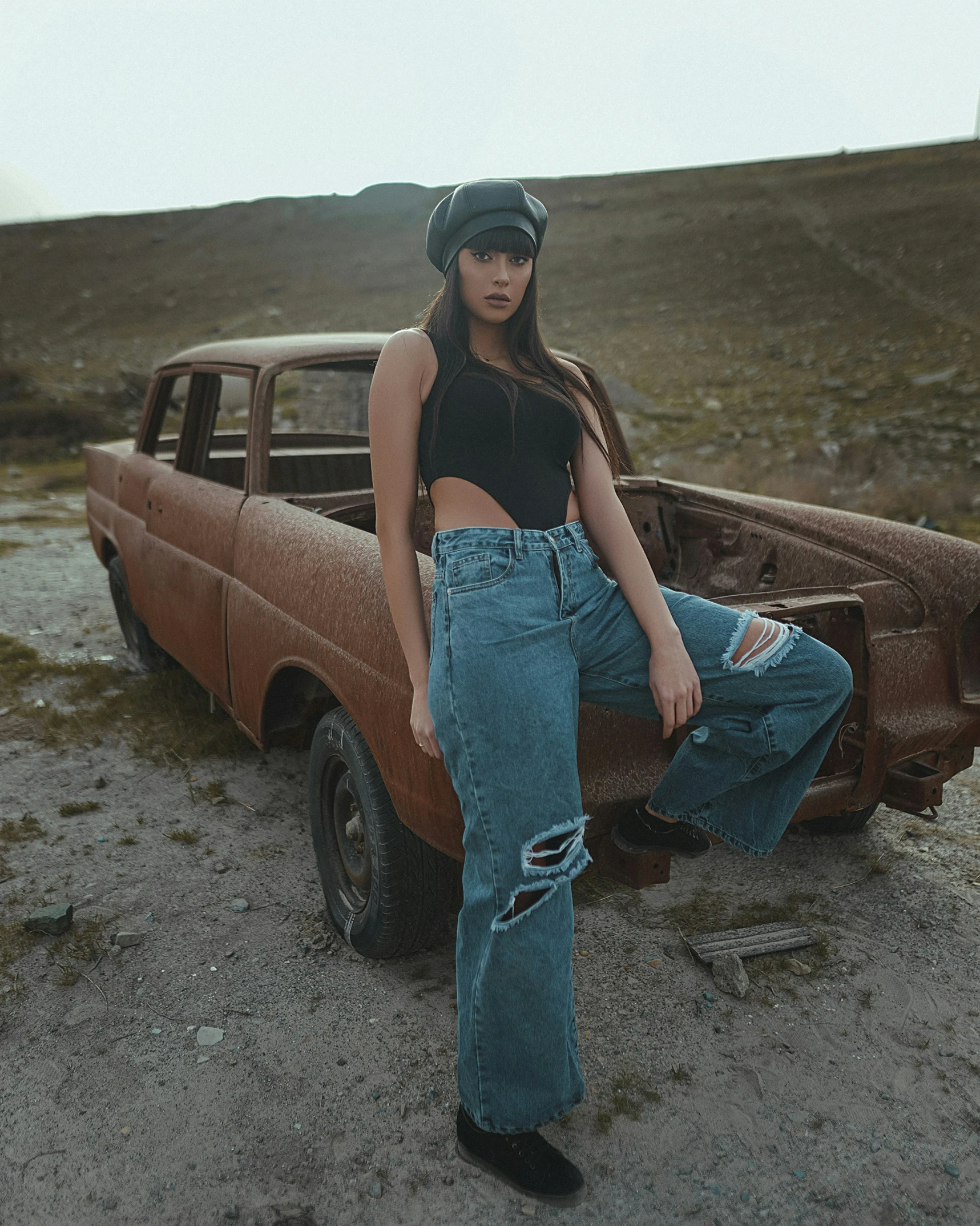 a woman wearing wide legged jeans and boots leaning on a rusted pickup truck