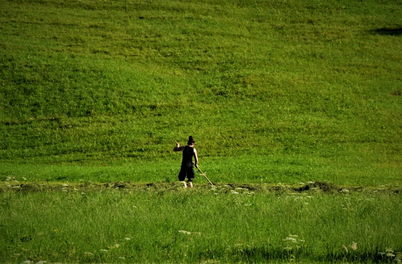 man holding his hand out as he walks along a green hill