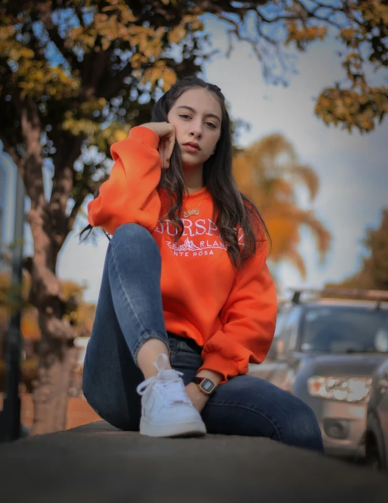 a beautiful young woman sitting on the side of a road next to a car