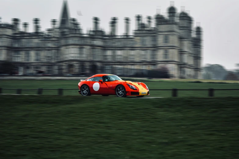 an orange car driving through a grassy field in front of a building