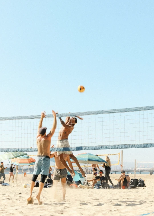 two men in shorts jumping into the air with a volleyball on a beach