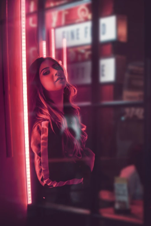woman with long hair standing behind a red neon light