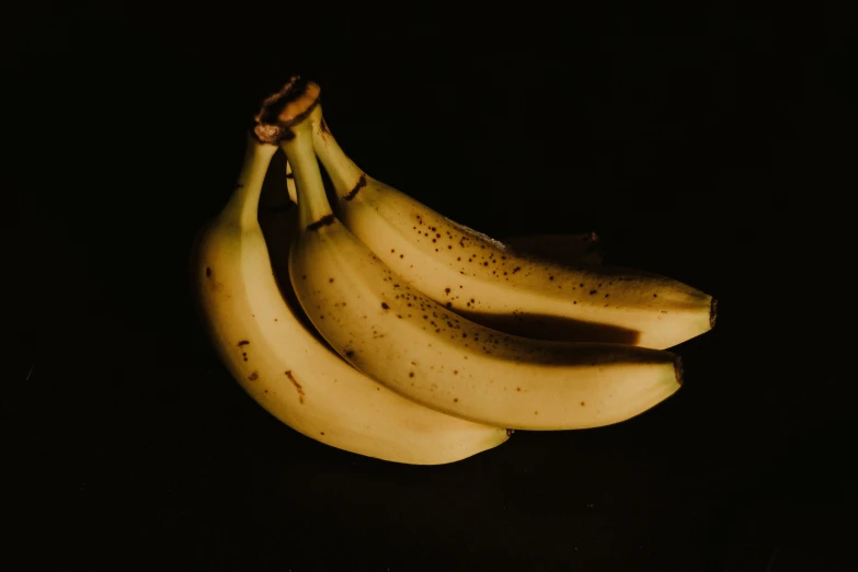 four ripe banana's on a dark surface