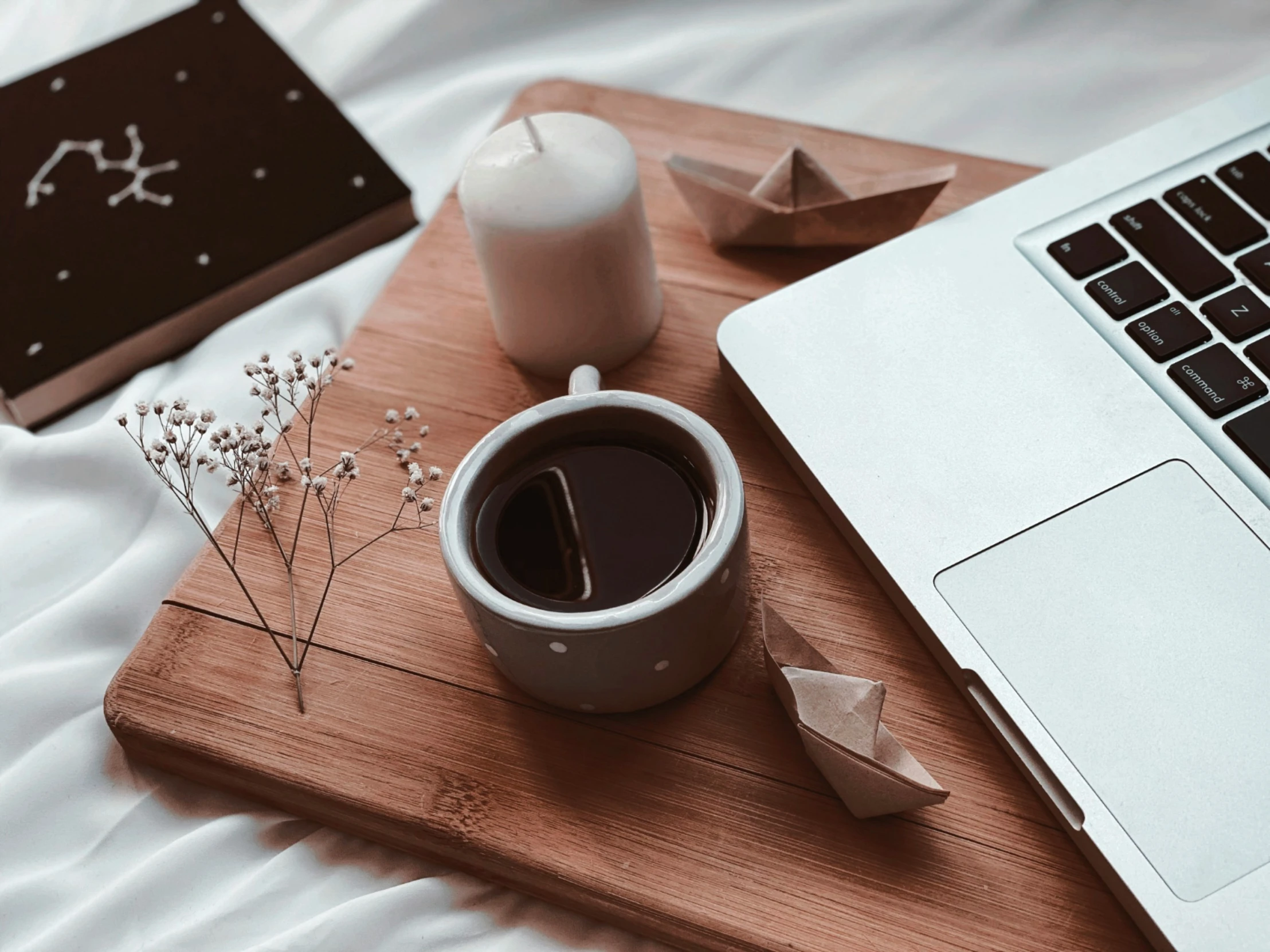 a coffee cup, pen, paper and laptop on top of a wooden  board