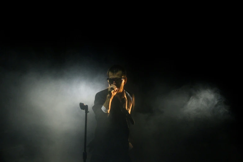 a man wearing glasses standing next to a microphone