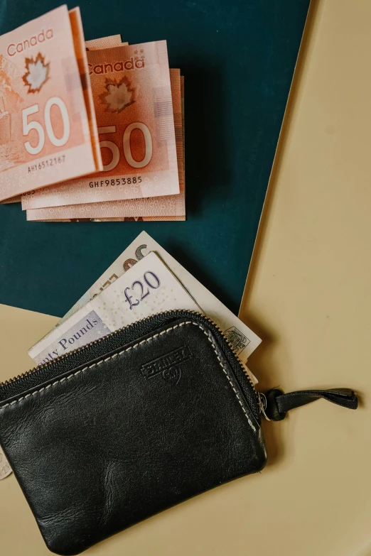 a small leather wallet with some fifty and fifty euros bills laying beside it