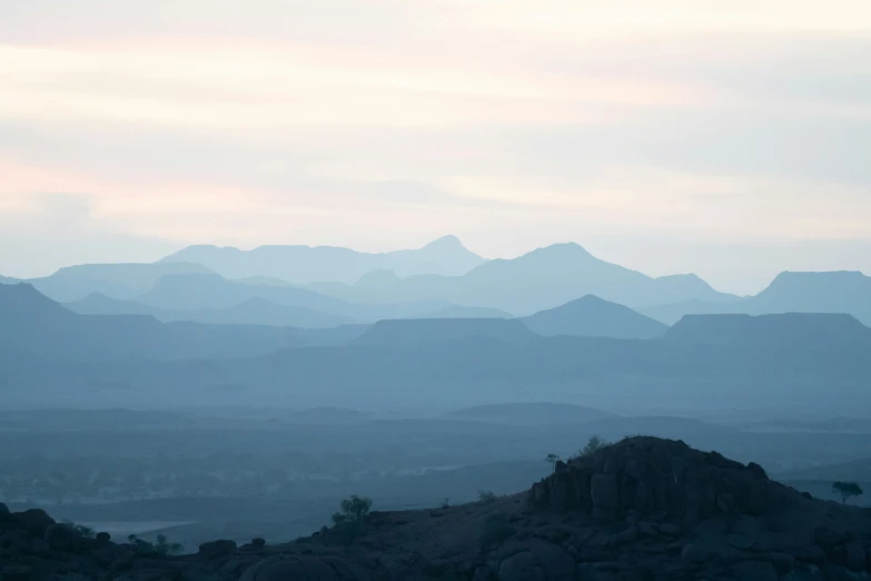 the tops of mountains are silhouetted against a pale blue sky