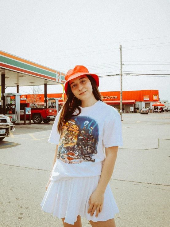 a girl wearing an orange hat standing in front of a gas station